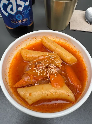 Bol de tteokbokki, pâtes de riz épicées, servi avec une bière Cass